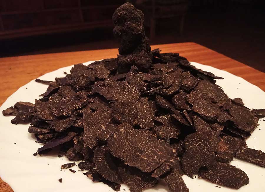 Láminas finas de trufa negra fresca amontonadas sobre un plato blanco.